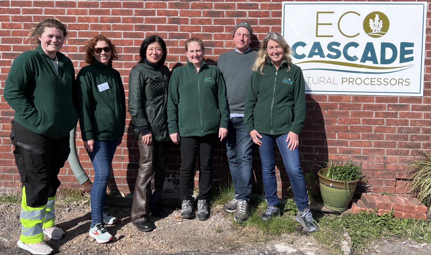 Group of people standing and smiling next to an Eco Cascade poster.