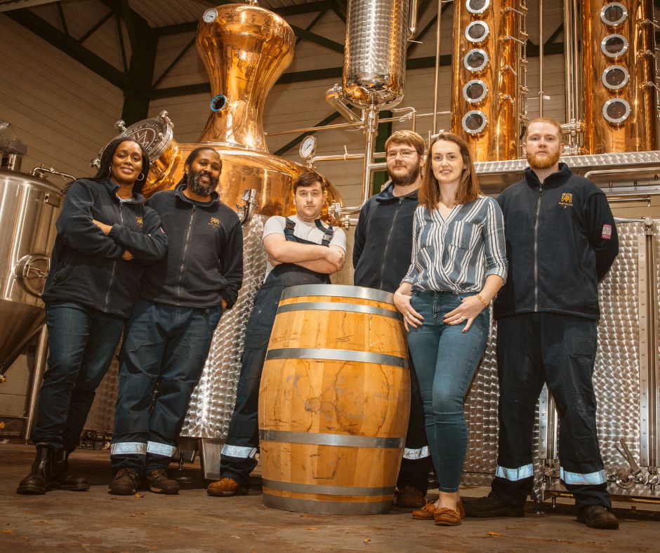 Group of people standing in front of rum distilling equipment.